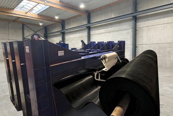 Rouleau de bande transporteuse en caoutchouc posé devant un châssis de convoyeur bleu dans un atelier