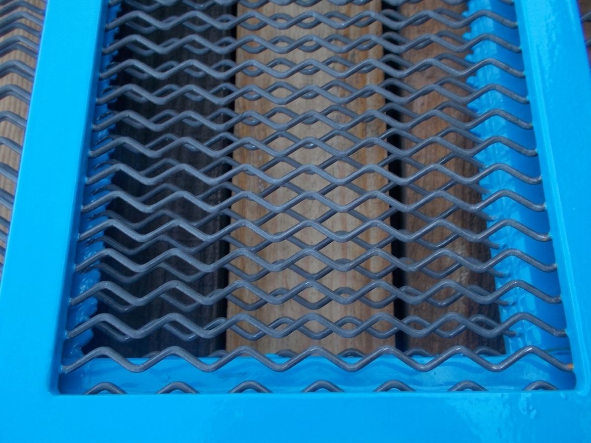 Toile en acier anti-colmatante à fils ondulés dans un cadre bleu, posée sur des planches