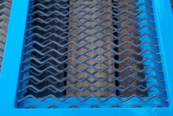 Toile en acier anti-colmatante à fils ondulés dans un cadre bleu, posée sur des planches