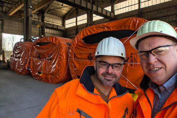 Deux techniciens en tenue orange devant des bobines de bande transporteuse emballées en bâche orange