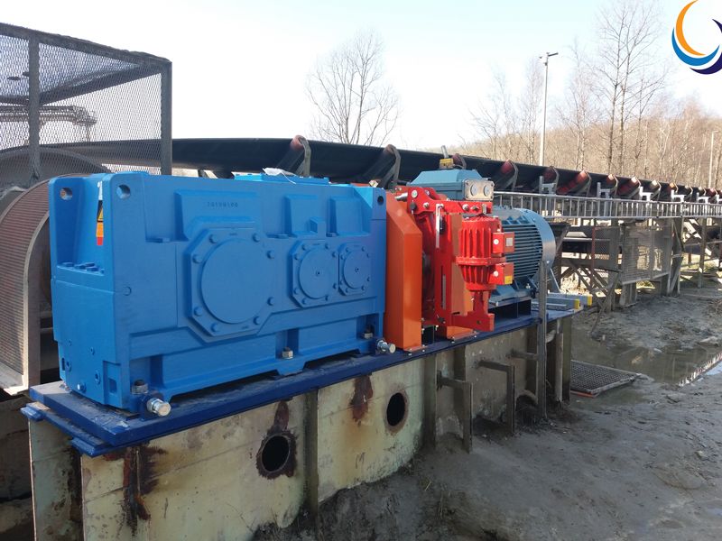 Réducteur à engrenages bleu, frein rouge et moteur électrique entraînant un convoyeur à bande en extérieur