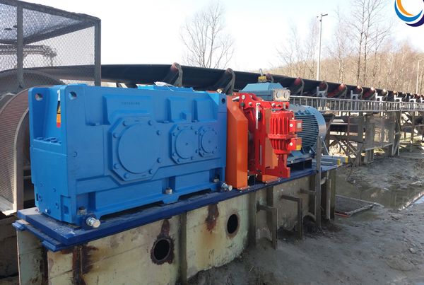 Réducteur à engrenages bleu, frein rouge et moteur électrique entraînant un convoyeur à bande en extérieur
