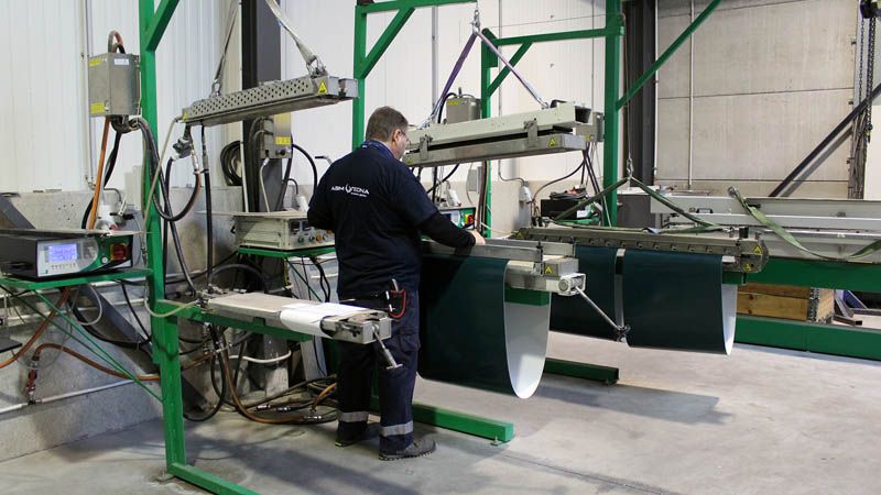 Opérateur jonctionnant une bande légère verte sous les presses de l'atelier PVC-PU
