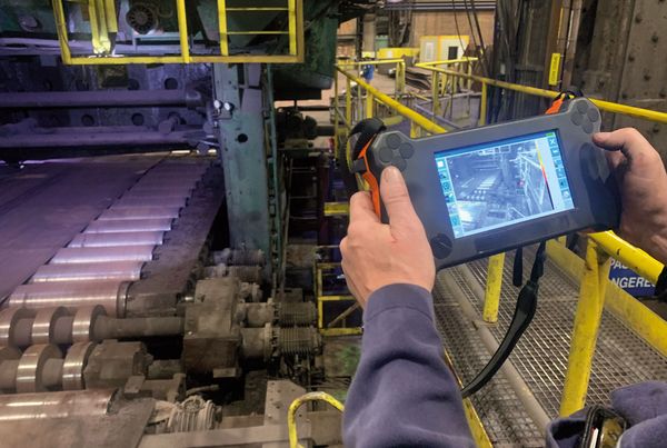 Technicien tenant une caméra ultrason et thermique portable devant une ligne de rouleaux industriels