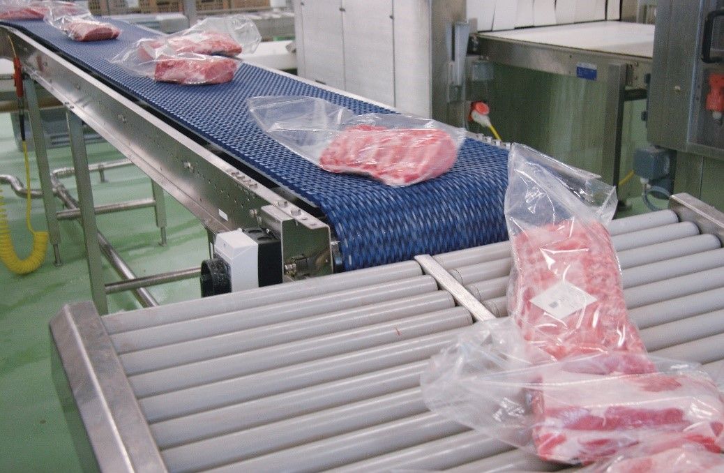 Bande modulaire bleue transportant des sachets de viande sur une ligne agroalimentaire