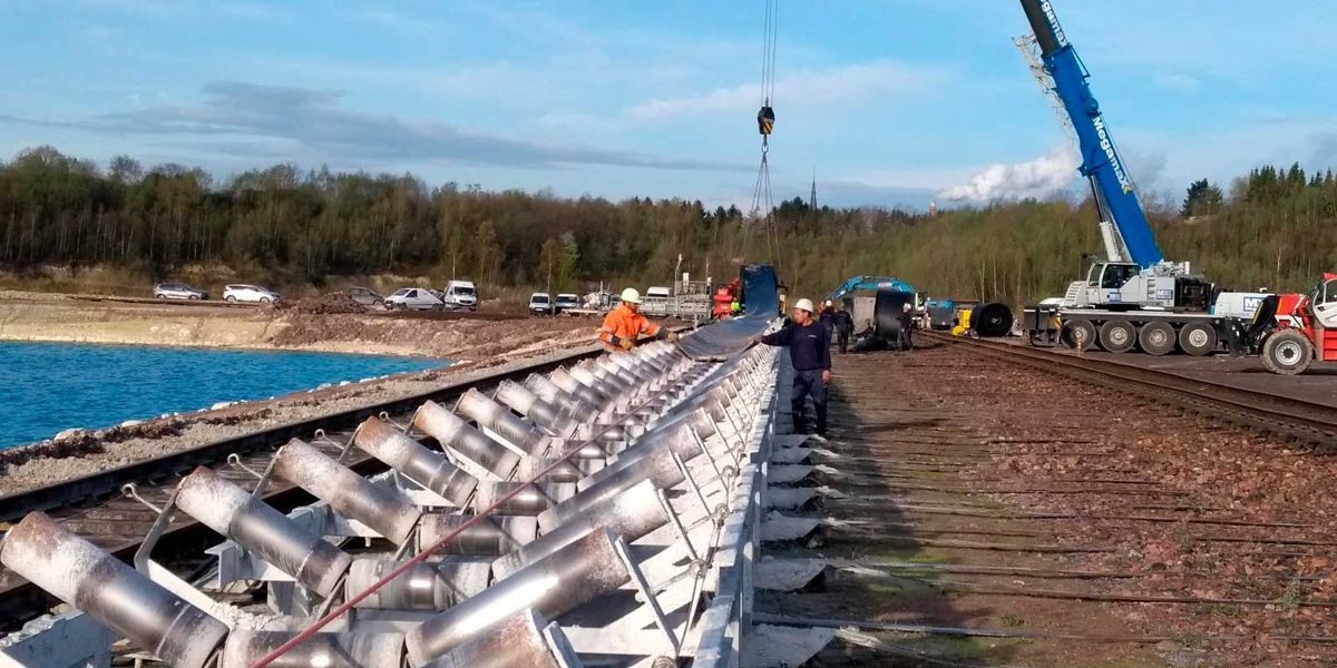 Team legt een transportband op een lange rollentransporteur, met kraan, aan de rand van een waterplas