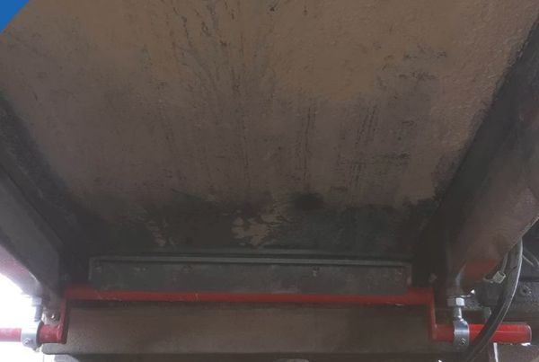 Racleur Brelko sur mesure : lame noire sur support rouge, fixé sous une trémie