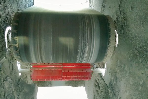 Brosse à lamelles rouges installée sous le tambour d'un convoyeur à bande, vue en contre-plongée