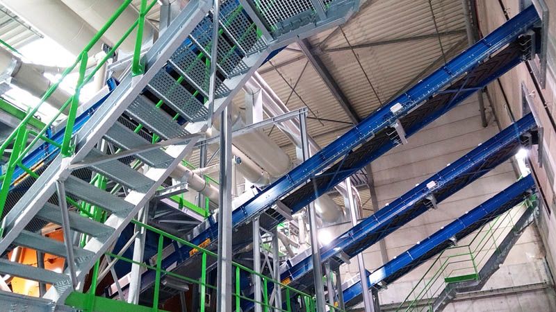 Convoyeurs inclinés bleus sous un escalier métallique, dans un bâtiment industriel