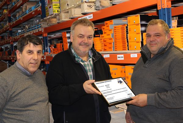 Trois hommes dans un magasin de roulements, l'un tient le certificat Timken Bearing Certification remis à ABM TECNA