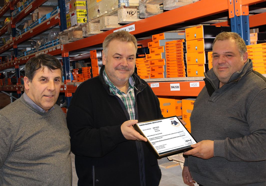 Drie mannen in een lagermagazijn, een van hen houdt het Timken Bearing Certification-certificaat voor ABM TECNA vast