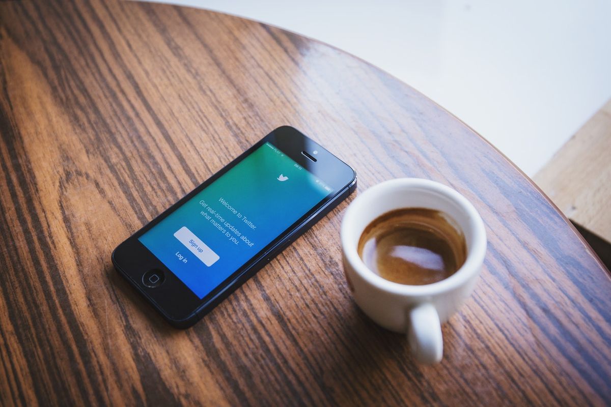 Smartphone met het startscherm van Twitter naast een kopje koffie op een houten tafel