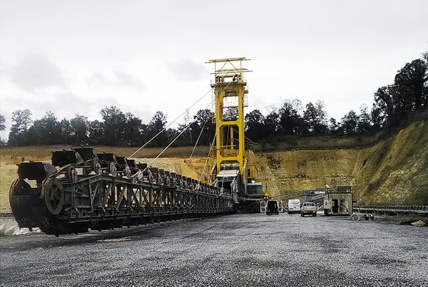 Excavatrice d'extraction en carrière : chaîne de godets posée au sol devant un portique jaune, logo ABM TECNA