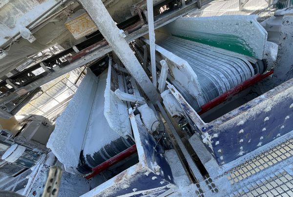 Deux racleurs de bande à lames polyuréthane installés sous deux convoyeurs jumeaux, couverts de poussière blanche