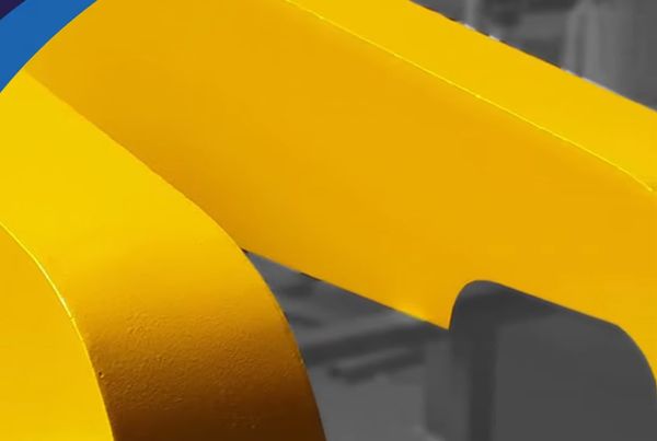 Détail d'un garant jaune protégeant une transmission par courroie, sur fond d'atelier gris