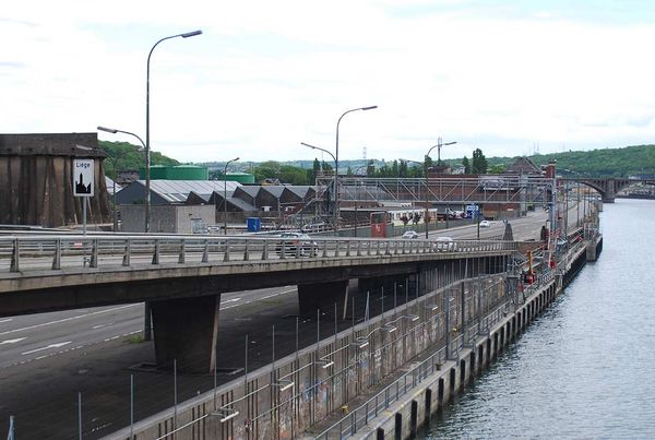 Autoroute urbaine surélevée le long d'un fleuve, panneau d'entrée de Liège, collines et pont au loin