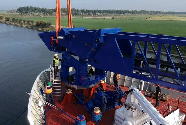 Montage d'un convoyeur à bande bleu levé par grue sur le pont d'un navire, trois ouvriers en gilet de sécurité