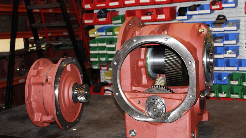 Geopende behuizing van een SIMOGEAR-motorreductor op de werkbank, rondsel en tandwiel zichtbaar, bakken met onderdelen