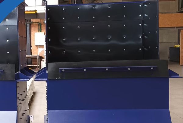 Trémie en acier bleu avec parois intérieures revêtues de plaques noires boulonnées, en atelier