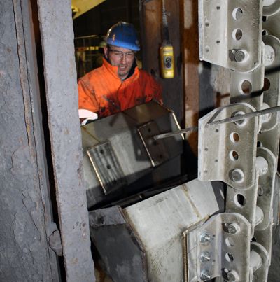 Technicien casqué à l'intérieur d'un élévateur à godets en inox, godets fixés sur la courroie