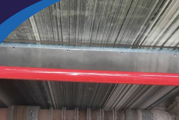 Lame de racleur SJC fixée sur un tube rouge sous une bande de convoyeur, au-dessus d'un tambour