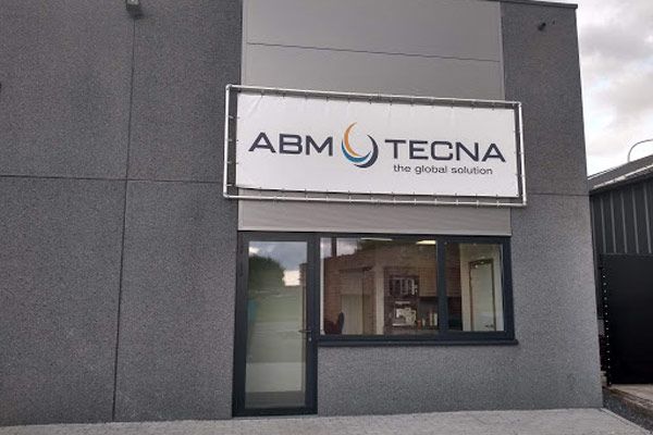 Façade du site ABM TECNA à Tournai : bâtiment gris avec grande enseigne sur la façade et porte vitrée
