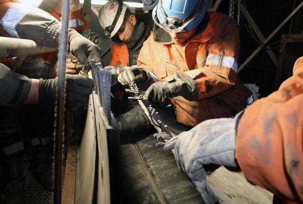 Techniciens en tenue de protection assemblant la bande d'un élévateur à godets, gants et casques