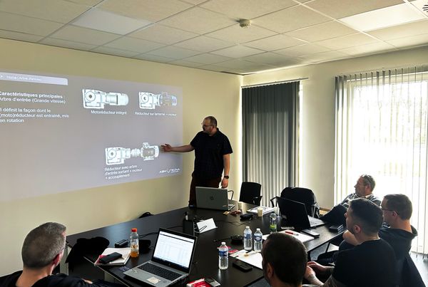 Formateur ABM TECNA devant un écran projeté sur les réducteurs et motoréducteurs, face à des clients attablés