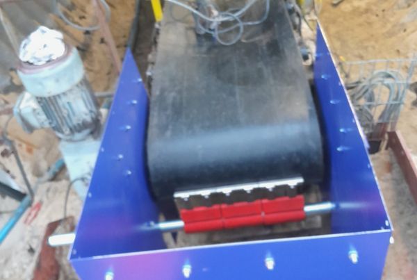 Transporteur tunnel vu de dessus : bande noire, racleur à lames rouges dans une structure bleue neuve